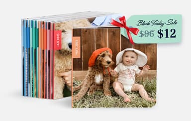 A stack of photo books stands upright, with the front book displaying a baby in a sun hat sitting on grass next to a dog in a red hat, both in front of a wooden fence.