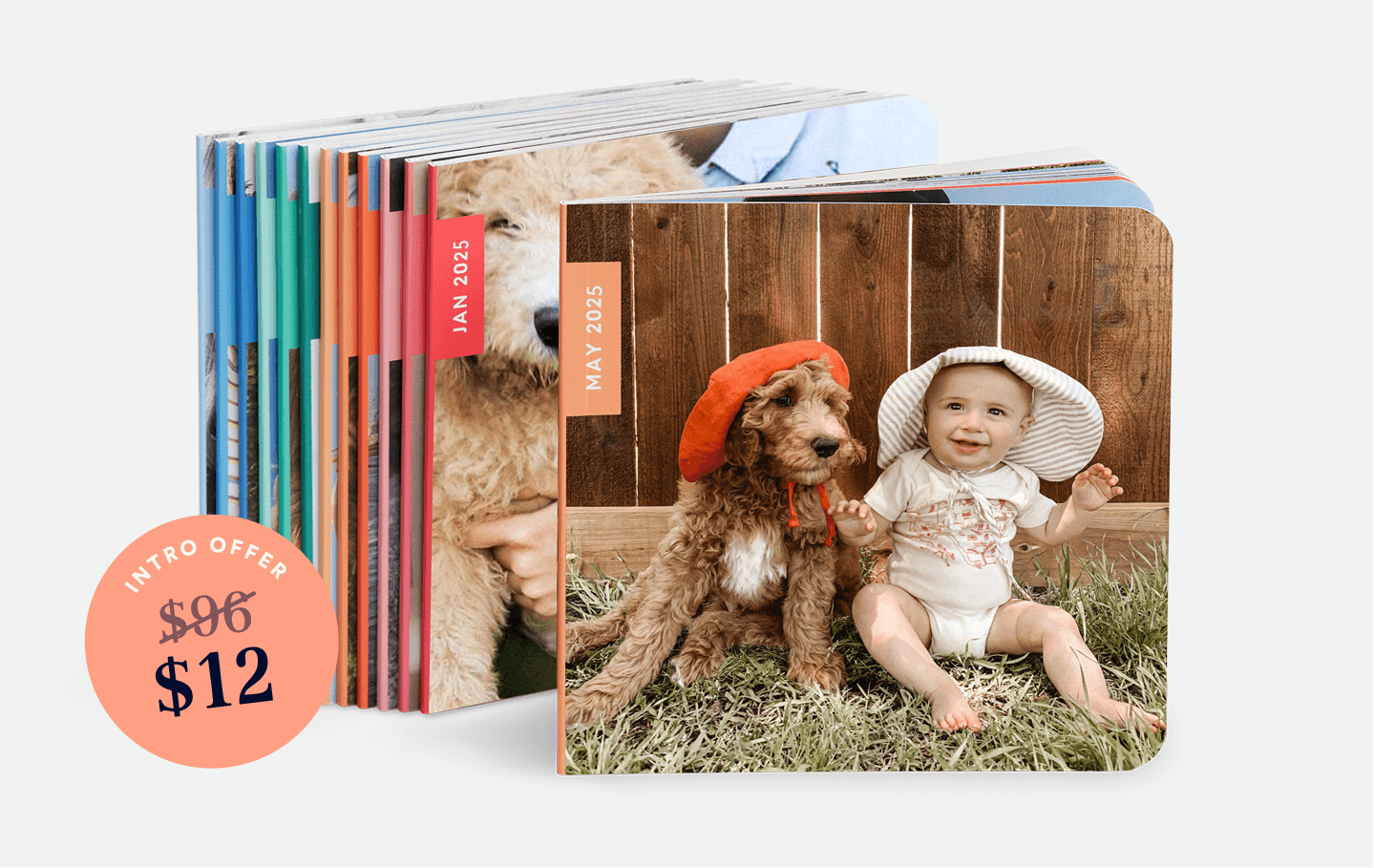 A stack of photo books stands upright, with the front book displaying a baby in a sun hat sitting on grass next to a dog in a red hat, both in front of a wooden fence.