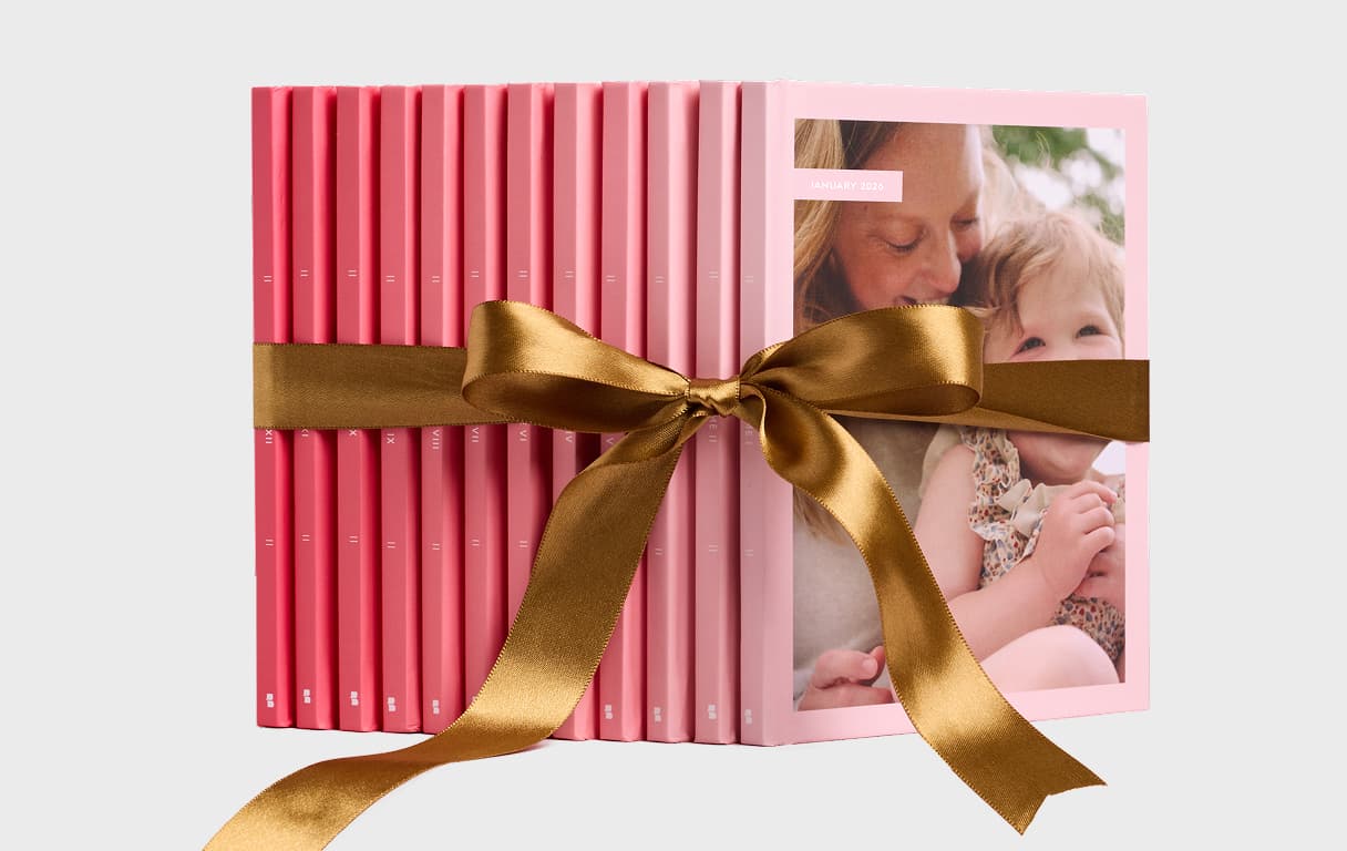 A fan display of monthly photo books tied with a ribbon next to a gift card labeled “One Year of Monthbooks,” highlighting the 12-month photo book gift collection.