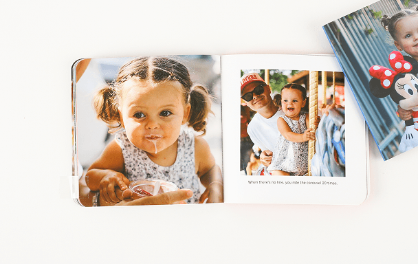 Open photo book showing a young child eating ice cream on one page and riding a carousel with an adult on the other, with a Minnie Mouse image partially visible nearby.