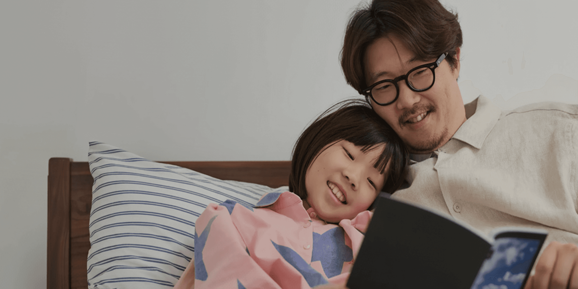 Father and daughter reading a Monthbook together in bed