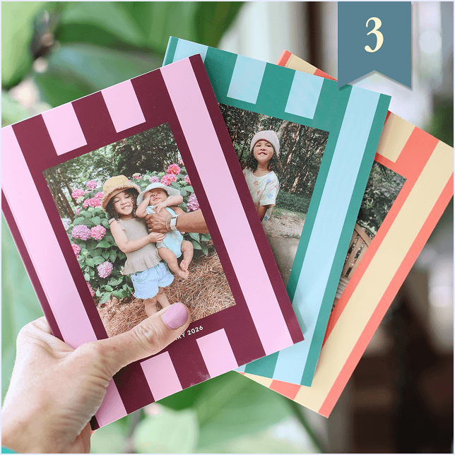 Hand holding a fan of three striped Monthbook covers with family photos on them