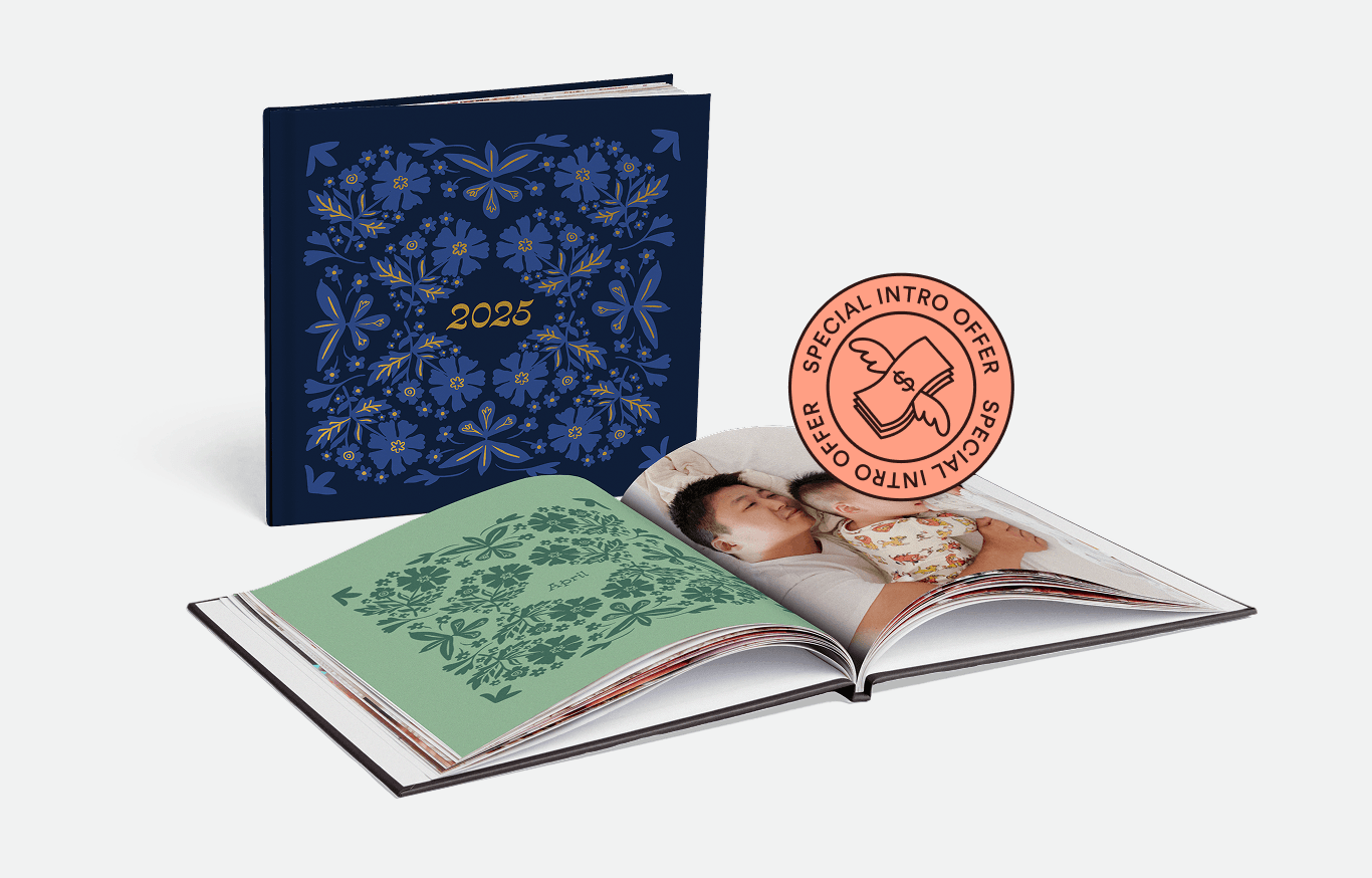 A blue 2025 photo book with floral design stands beside an open page showing a father and child.
