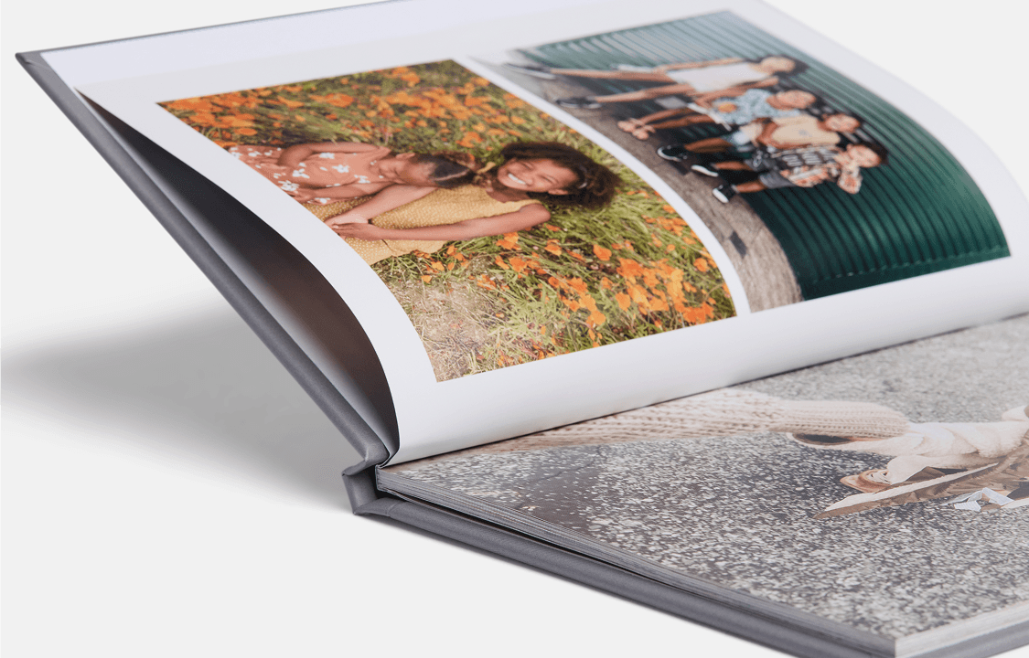 Open photo book showing diverse children in colorful outfits. One page features kids on grass with orange flowers, another shows kids sitting in front of a green wall.
